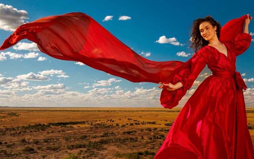 Nina Korbe, OQ Young Artist stands on Winton landscape wearing a red dress.